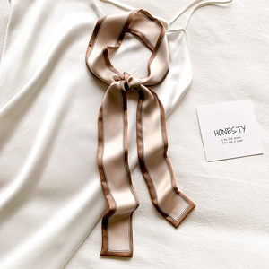 Détail d'un foulard en soie champagne noué sur une robe blanche à fines bordures