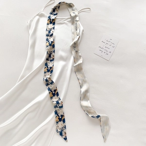 Detail eines schmalen Seidenschals mit Blumenmuster und weißem Satin-Kleid im Set