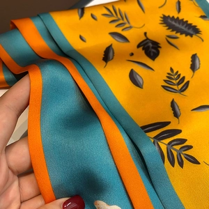 Macro shot of long silk scarf showing vibrant yellow leaf print and blue contrast border