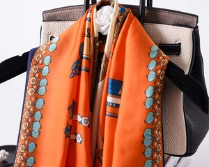 Close-up of orange silk scarf with vintage carriage pattern draped over a leather handbag