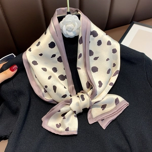 Detail of a beige silk scarf with black spots and lavender borders tied on a black knit