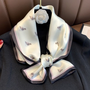 Detail view of a silk scarf with horse print and contrast borders on a black sweater