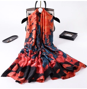 Detail of silk scarf with floral print in red and navy draped over a beige handbag