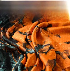 Close-up of silk scarf showing orange and dark green abstract pattern and soft texture