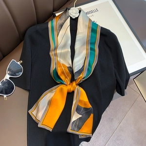 Detail of a thin silk scarf with geometric print tied to a black knit top