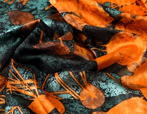 Close-up of silk scarf with orange and teal abstract prints showing satin texture and draping