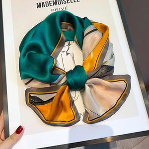 Detail of silk-like scarf with geometric print and gold lines tied in a bow shape