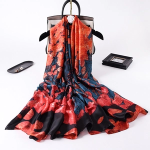 Fashionable floral print silk scarf in red and blue draped over a handbag on white background