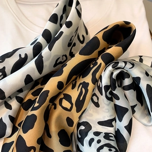 Close-up of leopard print satin scarves in beige and grey with glossy silk texture