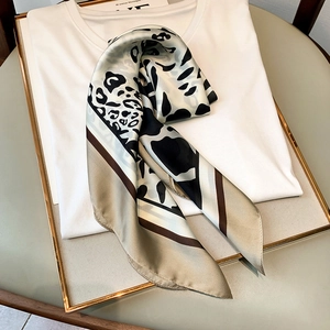 Detail of leopard print silk scarf folded on white shirt with luxury golden frame accents
