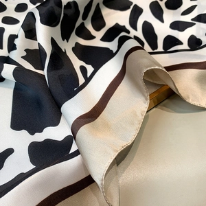 Detailed close-up of leopard print silk scarf fabric with sleek satin finish and brown edges