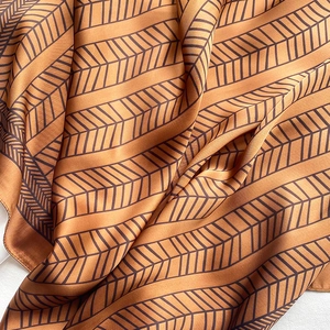 Macro shot of caramel silk scarf showing herringbone pattern and delicate rolled edges