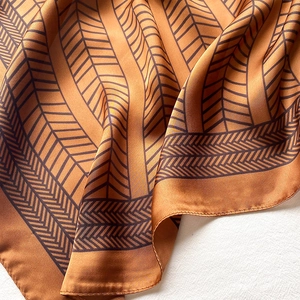 Macro detail of ochre silk scarf showing geometric pattern and fine stitching quality
