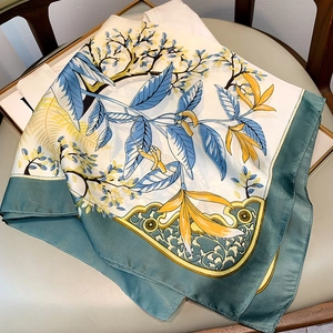 Close-up of floral silk scarf with dark green edges and satin finish on a leather chair