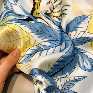 Detail shot of blue tropical leaf print on satin silk scarf with soft gloss and texture