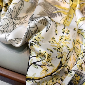 Close-up of silky floral neck scarf with yellow and grey leaf print on a leather chair