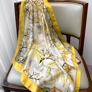 Detailed texture of floral silk scarf draped on leather chair with yellow border accents