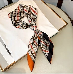 Détail d'une longue écharpe en soie pied-de-poule avec bordure orange sur chemise blanche