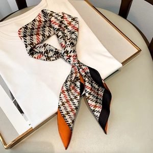 Détail d'un foulard en soie noué avec motif pied-de-poule orange et géométrique