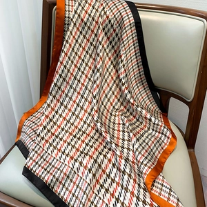 Détail d'un foulard en soie à motif pied-de-poule et bordure orange sur une chaise