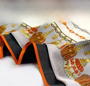 Gros plan détaillé sur les bords orange finement cousus du foulard en soie à chaînes