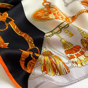 Détail d'un foulard en soie montrant des mors de cheval et des motifs de chaîne orange