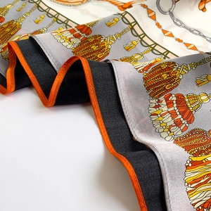 Détail de foulard en soie avec imprimé chaîne, pompons dorés et bords roulés orange vifs