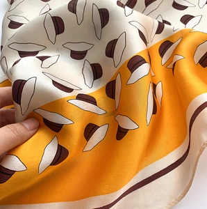 Gros plan d'un foulard en soie avec imprimés de chapeaux et texture satinée jaune et beige