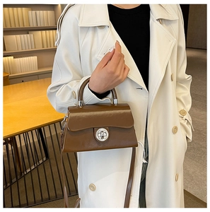 Sac boîte en cuir marron foncé avec fermoir argenté porté avec un trench-coat