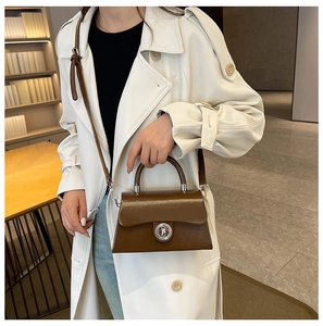 Sac trapèze marron avec fermoir métallique porté sur un trench-coat blanc