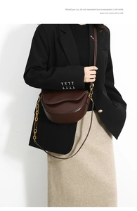 Close-up of dark brown leather saddle bag featuring a gold chain and wavy flap detail