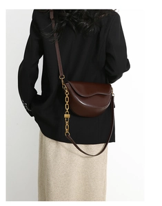Detail view of a vintage dark brown saddle bag featuring gold chain and leather strap
