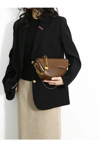 Brown leather saddle bag with gold chain strap shown on a model in a formal suit