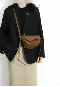 Brown saddle bag with gold chain and lock detail worn by model on white background
