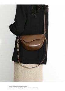 Detail of a brown saddle bag featuring a wavy flap design and gold chain link accents