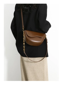 Detail of dark brown leather saddle bag with gold chain strap on black blazer
