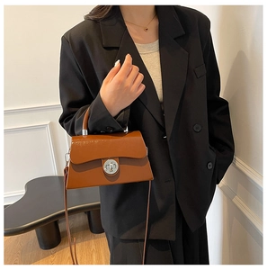 Sac bandoulière en cuir marron avec fermoir porté par un mannequin en blazer noir
