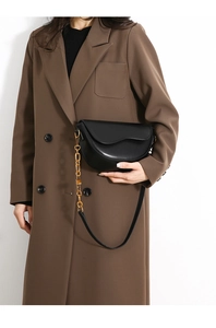 Detail of black leather half-moon saddle bag with thick gold chain and brown blazer