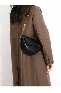 Detail of a black leather saddle bag with gold chain strap on a brown coat