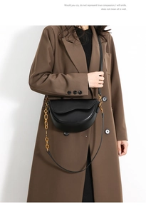 Detail of a black crescent saddle bag with gold chunky chain strap on a model's shoulder