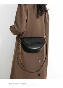 Detail of the black crescent saddle bag with gold chain strap on a trench coat