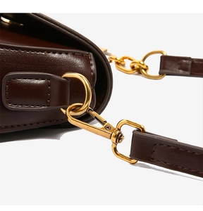 Detailed close-up of retro gold hardware and stitching on a dark brown leather bag