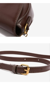 Detail of dark brown leather saddle bag with adjustable strap and gold metal buckle