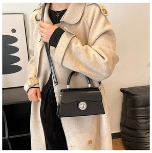 Détail du fermoir rotatif argenté sur le sac à bandoulière en cuir verni noir