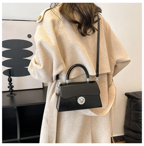 Détail d'un sac boîte noir minimaliste porté en bandoulière sur un manteau beige