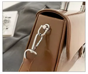 Gros plan du fermoir en métal argenté et de la sangle de ce sac box en cuir marron