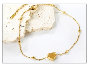Détail d'une chevillère en acier inoxydable doré avec pendentif cœur et perles sur pierre