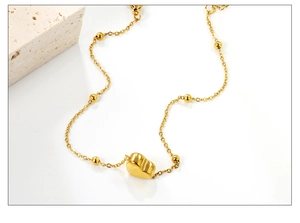 Macro d'un bracelet doré 18K avec pendentif coeur et perles rondes sur fond blanc pur