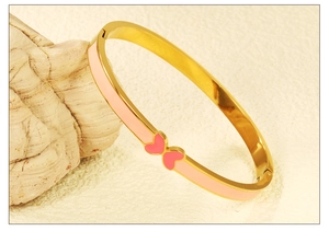 Close-up of gold hinged bangle featuring pink enamel hearts on a marble stone base