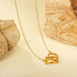 Collier doré à double anneau entrelacé avec texture organique posé sur une pierre naturelle